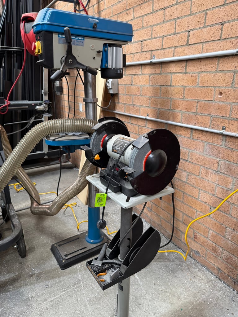 Blue and silver drill press with cutting wheel mounted against brick wall, with hose and yellow power cord visible