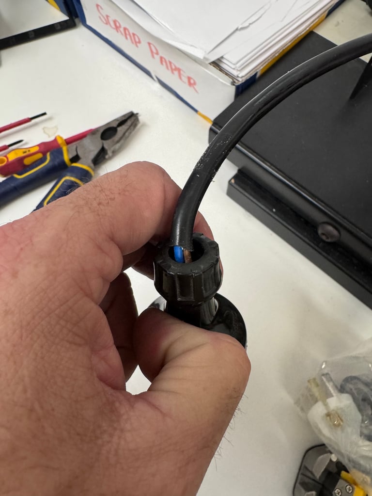 Hand holding a black electrical connector with a blue wire terminal on a workbench with tools and documents