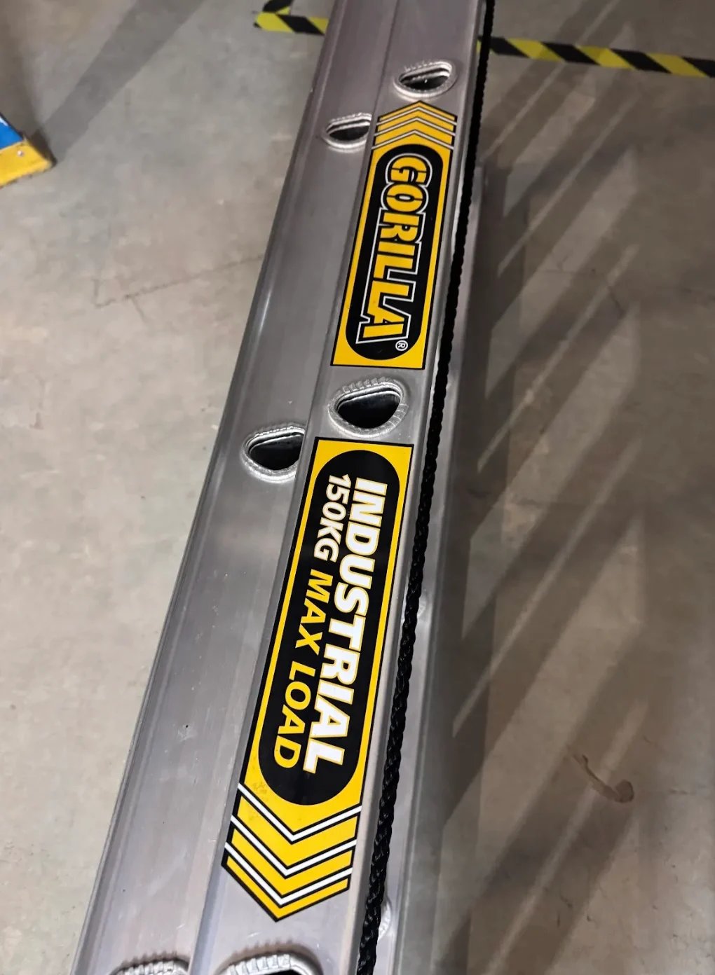Close-up of an industrial spirit level with yellow and black branding labels and measurement markings on gray metal body