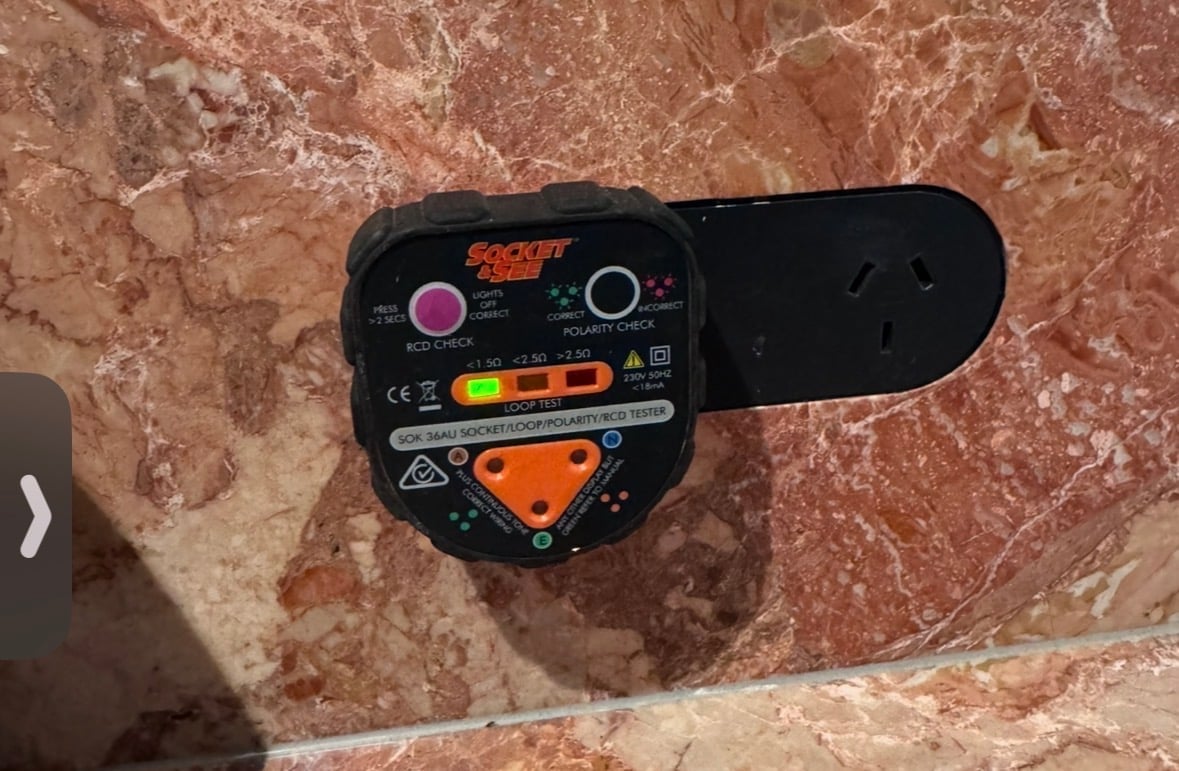 Black digital level tool with orange and purple buttons on terracotta tile floor