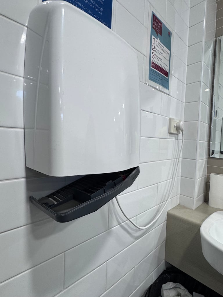 White automatic paper towel dispenser mounted on tiled bathroom wall above black drip tray