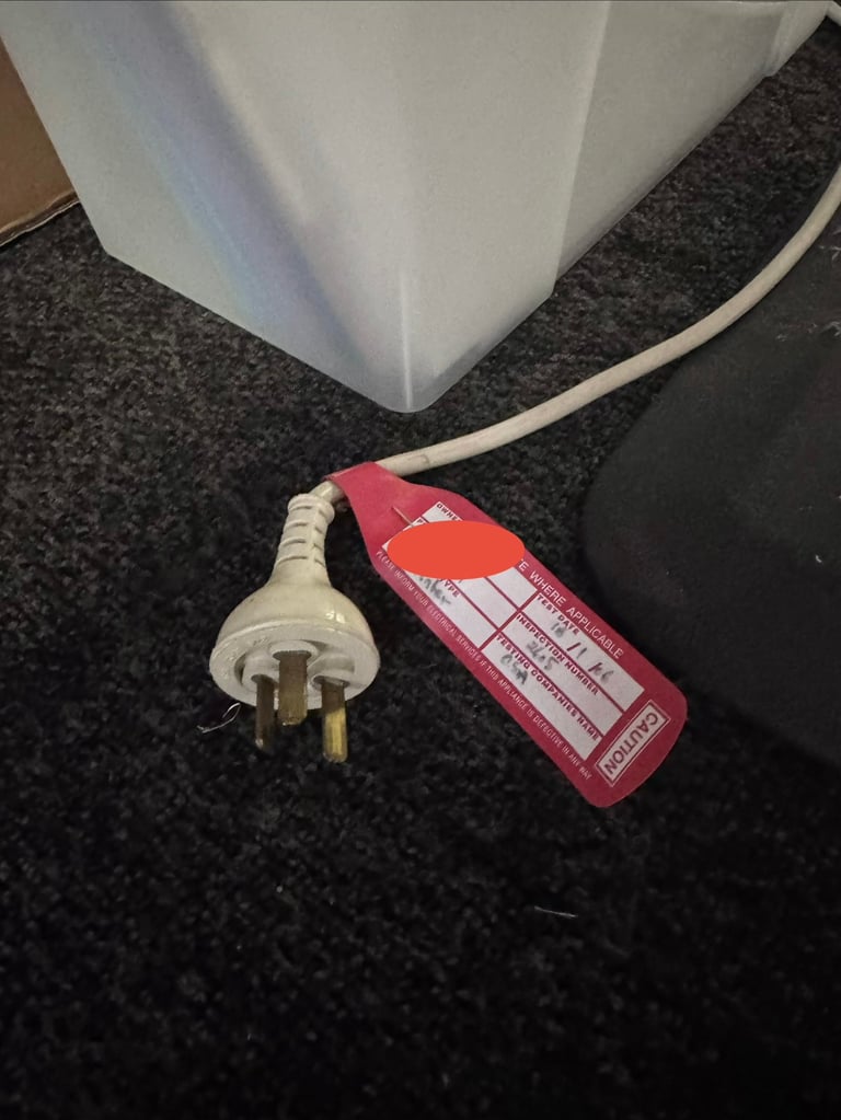 White electrical cord with red power strip on dark carpeted floor next to white appliance