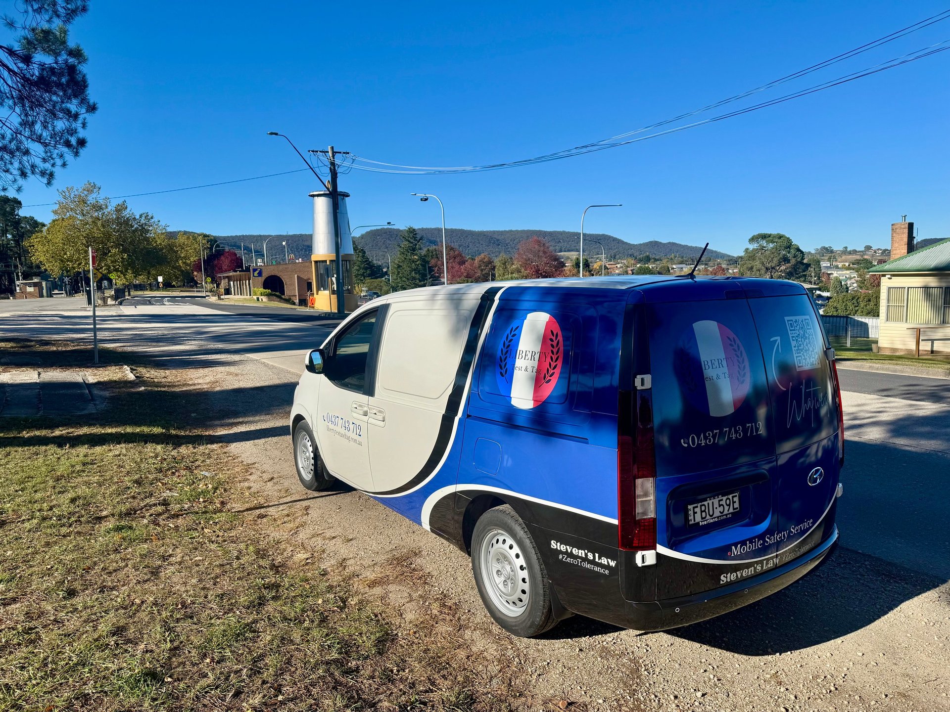 Blue and white van with open drivers side door parked on a residential street under clear blue sky