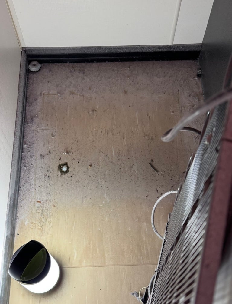 Overhead view of a dirty bathroom floor with a white toilet base and part of a radiator visible in the corner