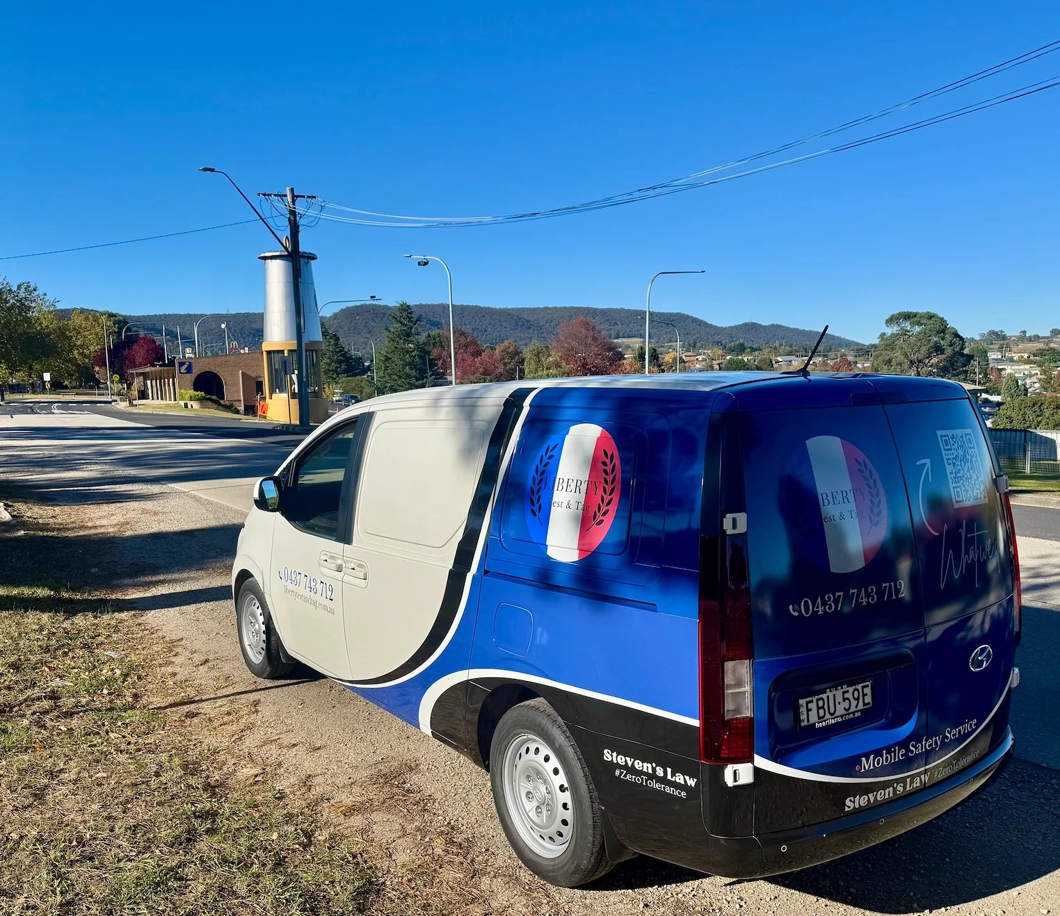 Two-tone blue and white van parked on a sunny day with mountains visible in the background
