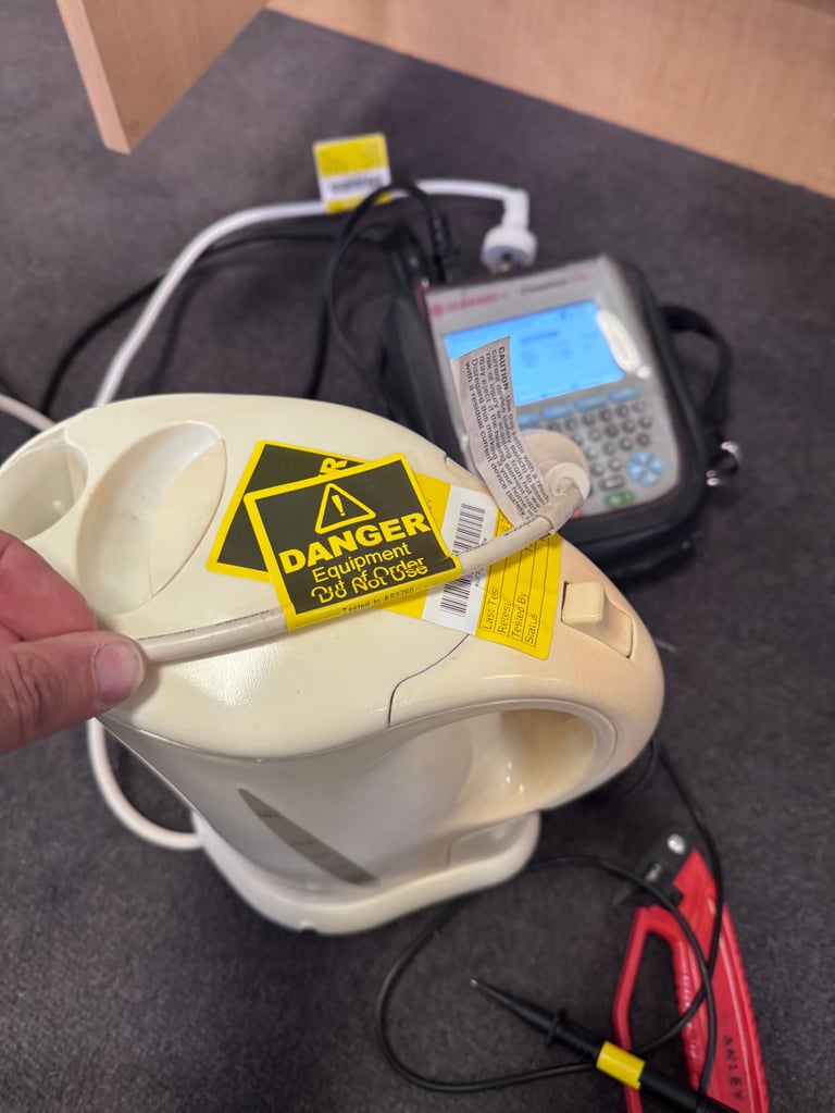Cream-colored electrical device with yellow Danger Equipment Out of Service tag attached, surrounded by cables and test equipment on dark floor