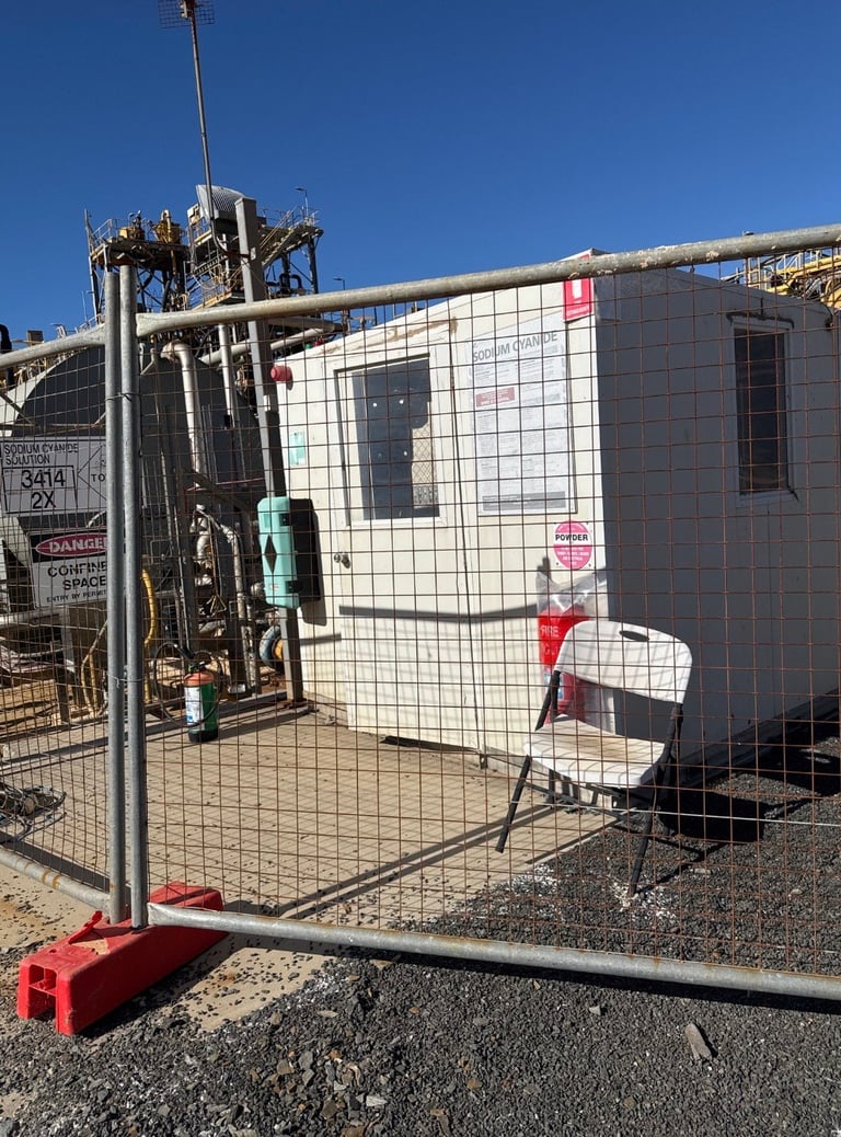 Construction site with temporary white metal-clad building, protective fencing, and industrial equipment under clear blue sky