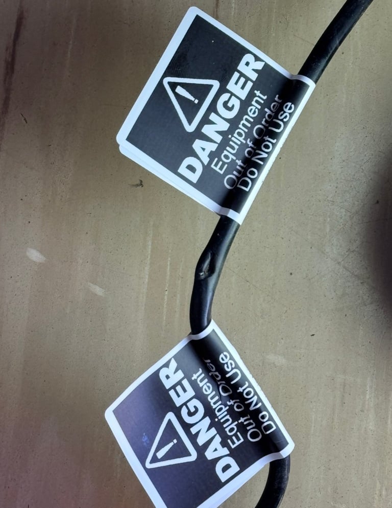 Black electrical cable with two white and black danger warning labels attached, indicating equipment hazard and do not use