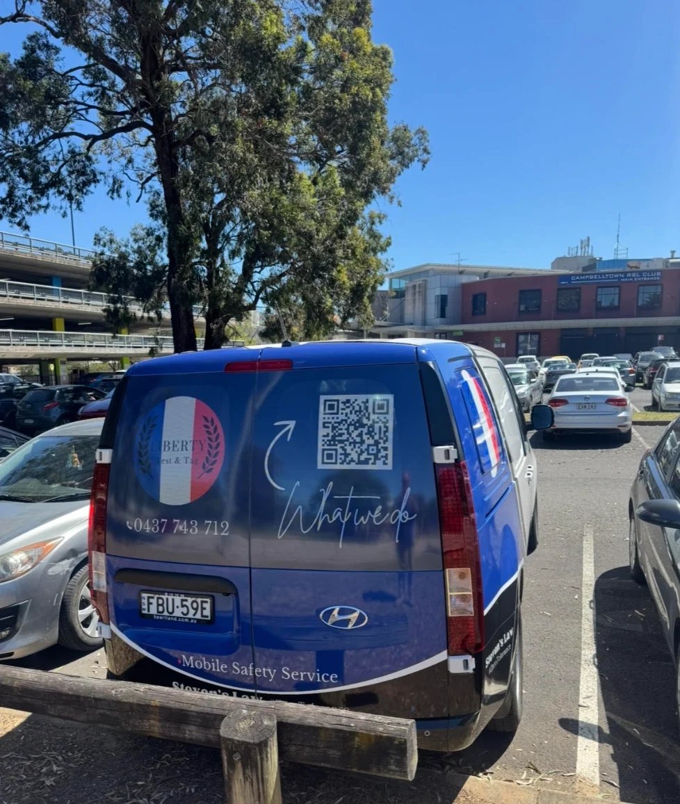 Historic brick church building with clock tower surrounded by green lawn, trees, and metal railings in daylight