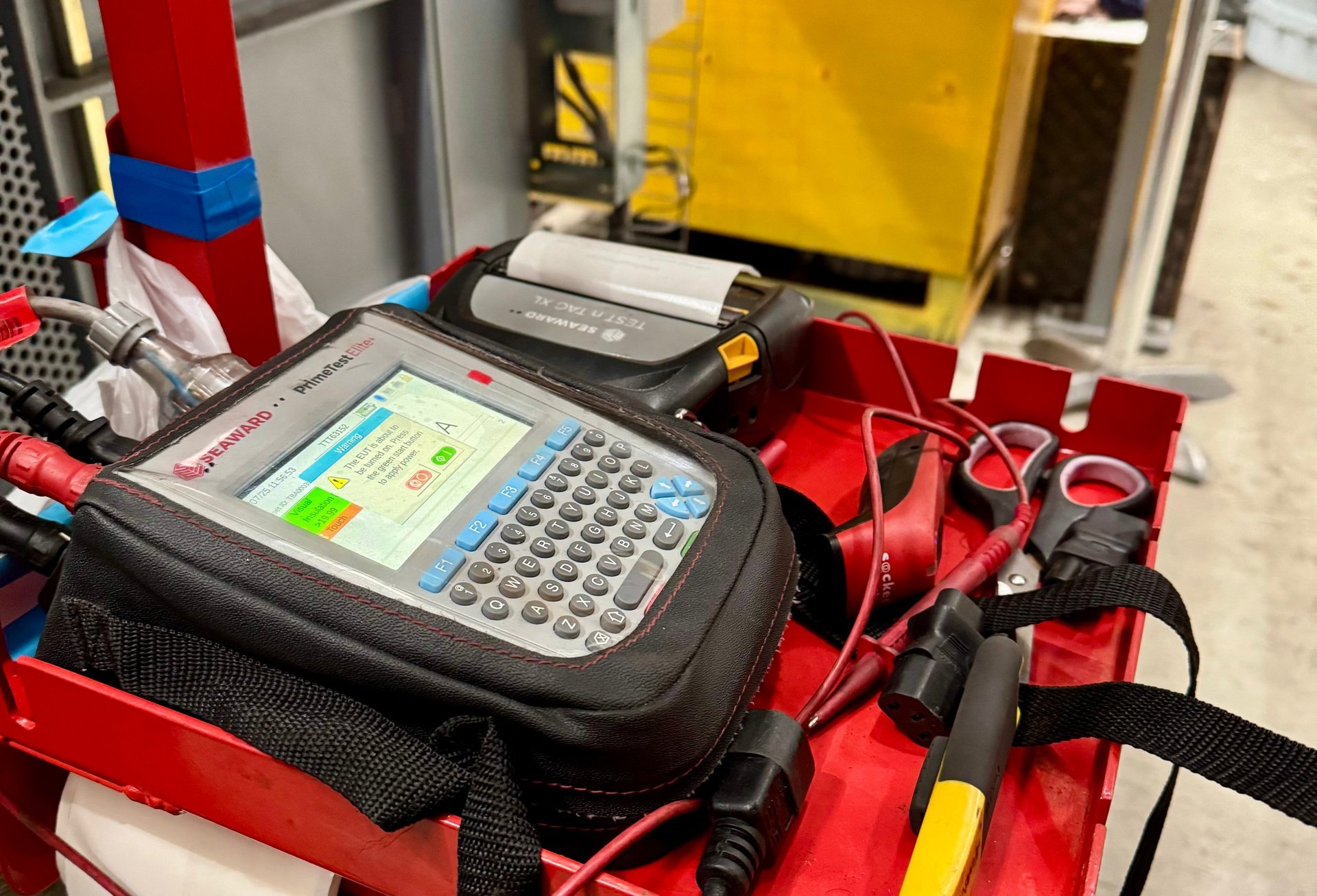 Handheld POS terminal with display screen mounted on red industrial equipment in warehouse setting