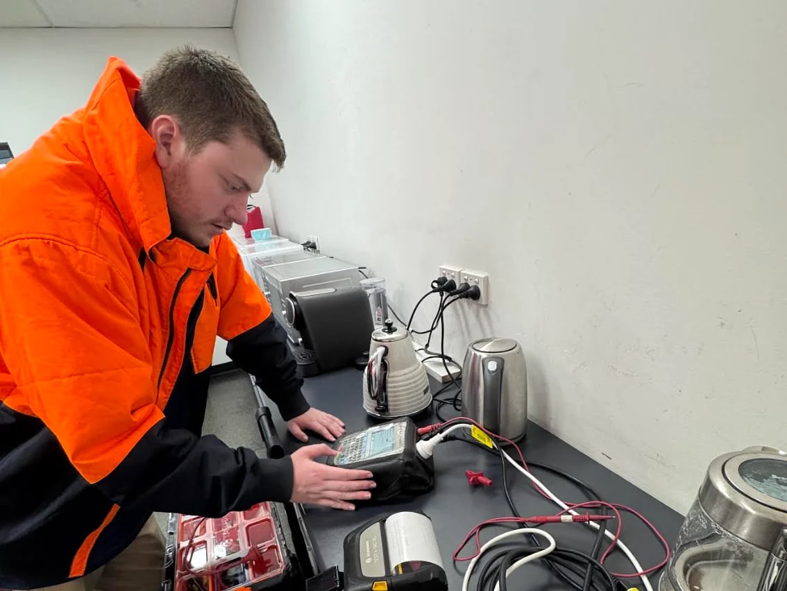 Technician in orange safety jacket working on electrical equipment and wiring at a control panel