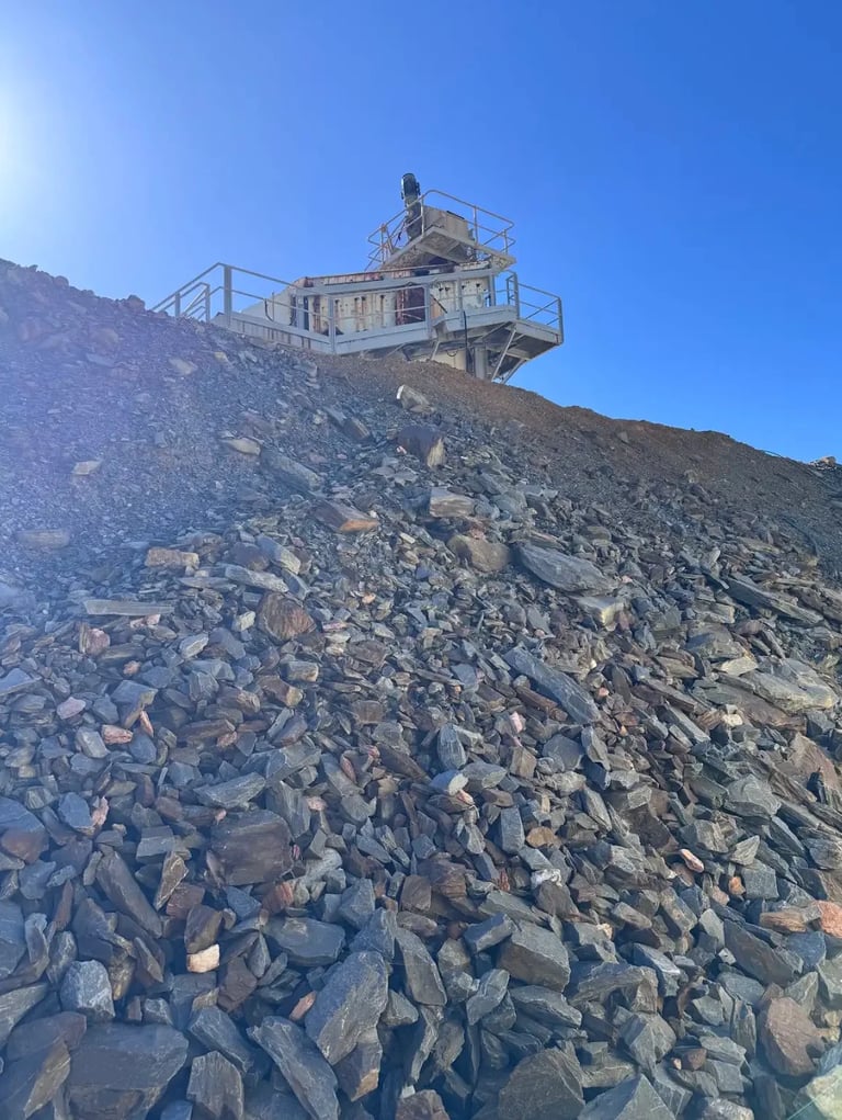 Industrial crushing plant on top of a rocky quarry hillside against clear blue sky