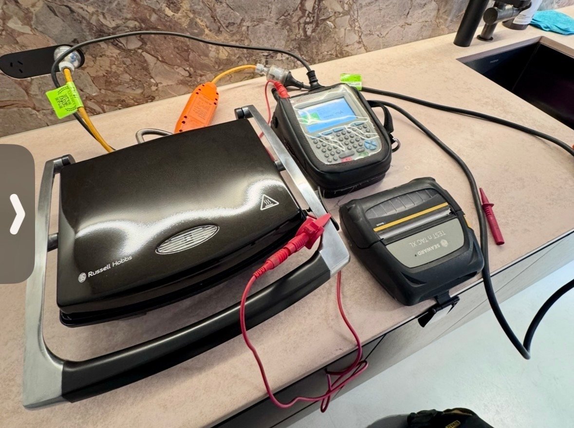 Testing equipment on a desk including a black device, two electronic meters with cables, and colorful testing probes