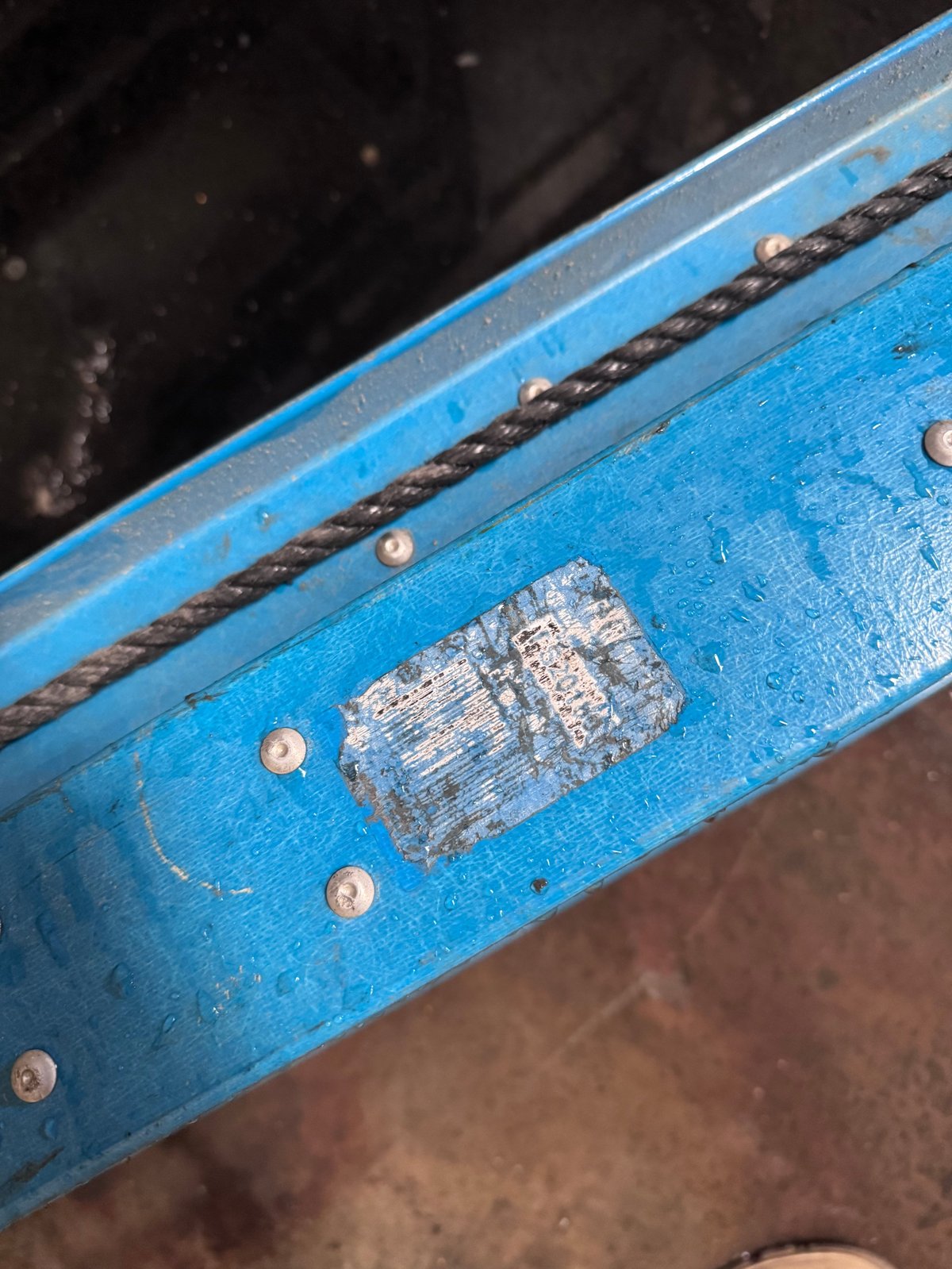 Blue metal beam or rail with rivets, worn label, and black chain detail on industrial equipment