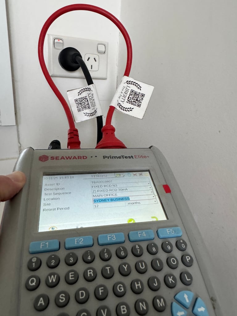SEAWARD PrimeTest Elite electrical testing device connected to a wall outlet with red cables and QR code labels