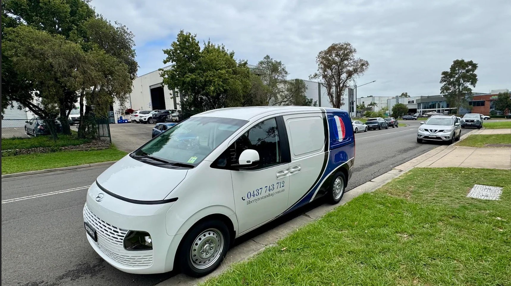 White taxi van parked on grass with red and blue stripe, Australian road with trees and vehicles in background
