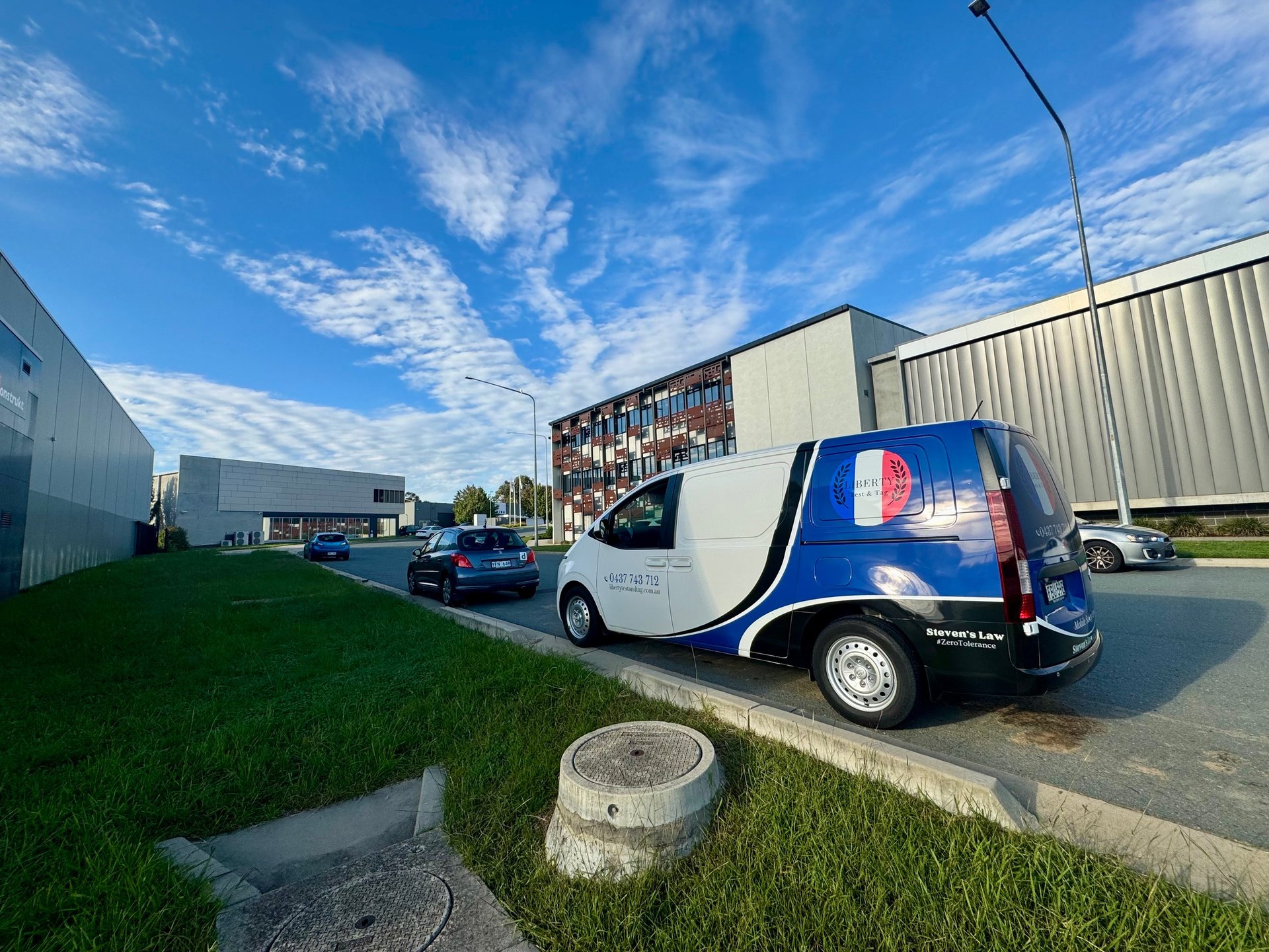 White and blue commercial van parked outside industrial building with clear blue sky