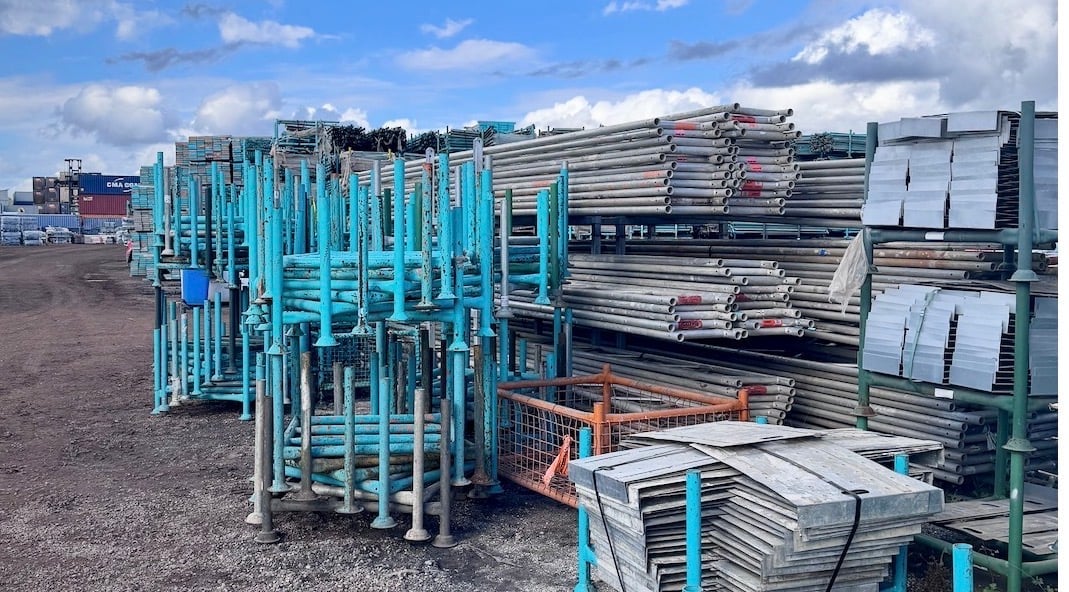 Industrial yard displaying stacked blue and silver metal livestock panels and gates under clear sky