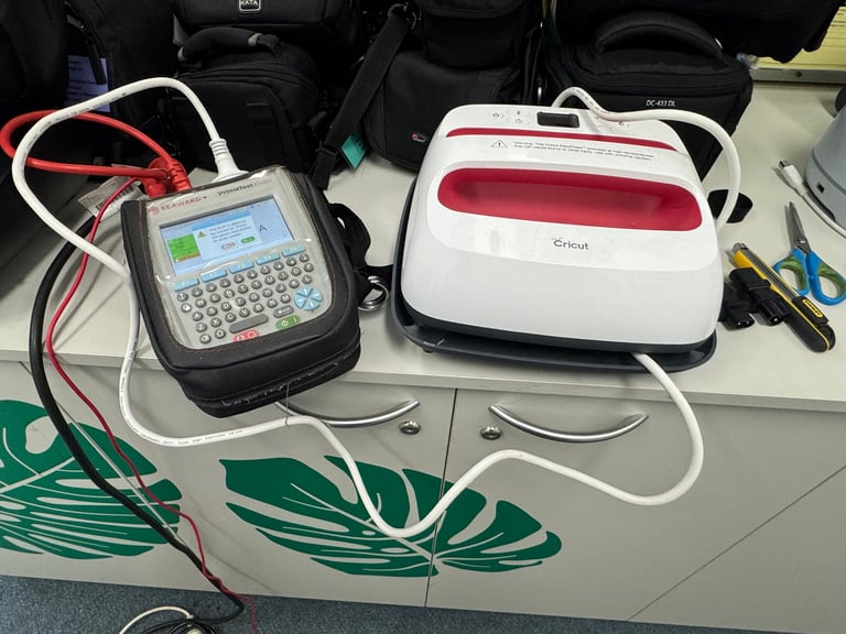 Lab equipment on white surface: portable device with LCD screen and red/white cables on left, white and red machine on right, with blue tools nearby