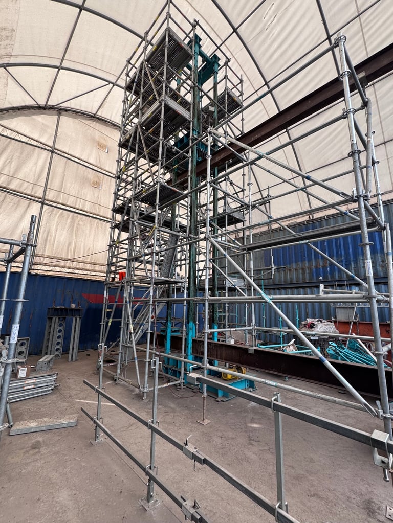 Tall metal scaffolding structure with stairs inside an industrial warehouse with white fabric roof and blue walls