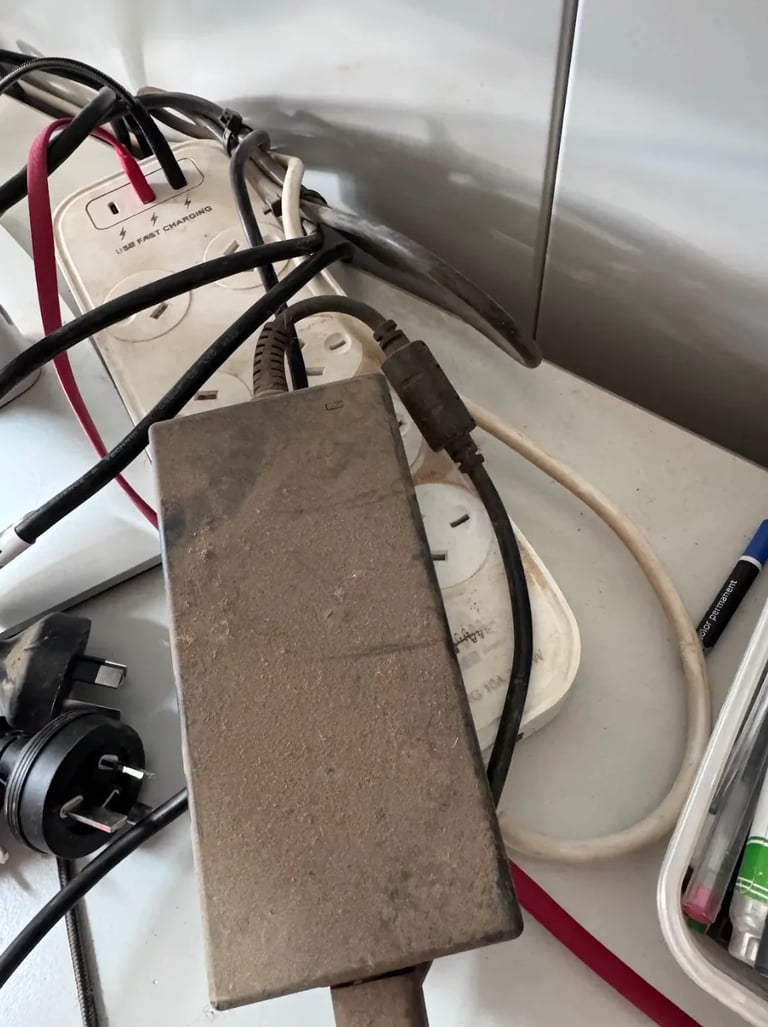 Dusty power adapter and tangled black cables connected to wall outlet and electrical devices