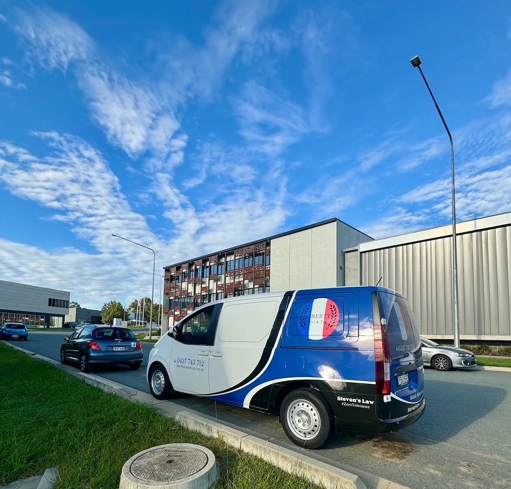 White and blue delivery van parked outside a modern industrial building under a clear blue sky