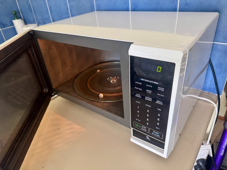 White microwave oven with open door on blue tiled kitchen counter, showing interior and control panel