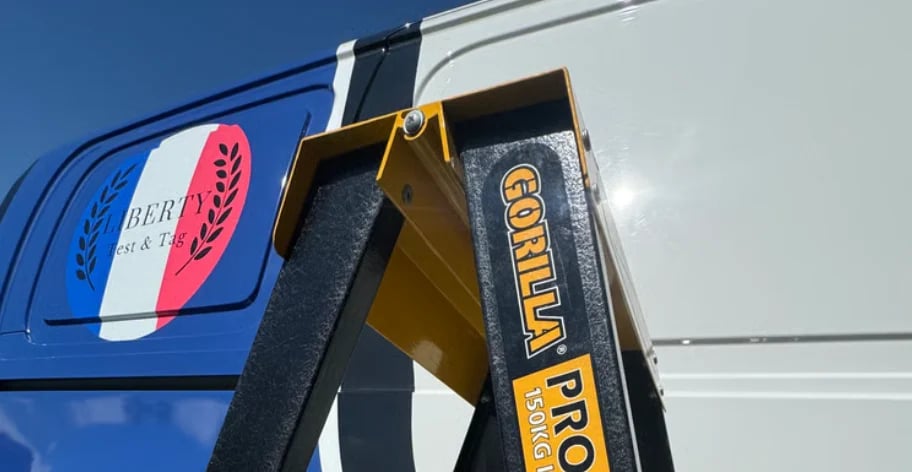 Gorilla Pro ladder leaning against a blue and white trailer with a red feather logo in bright sunlight