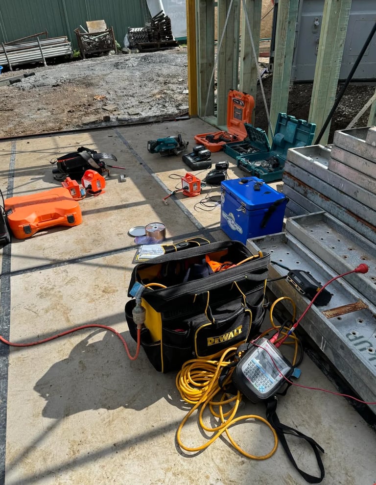 Construction work area with DeWalt tool bag, power tools, extension cords, and equipment scattered on concrete floor