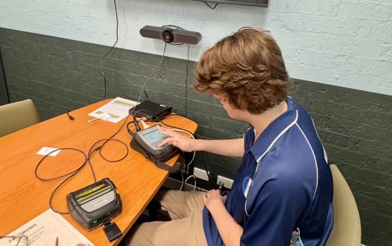 Person in blue polo shirt working with electronic equipment on orange table in classroom or lab setting