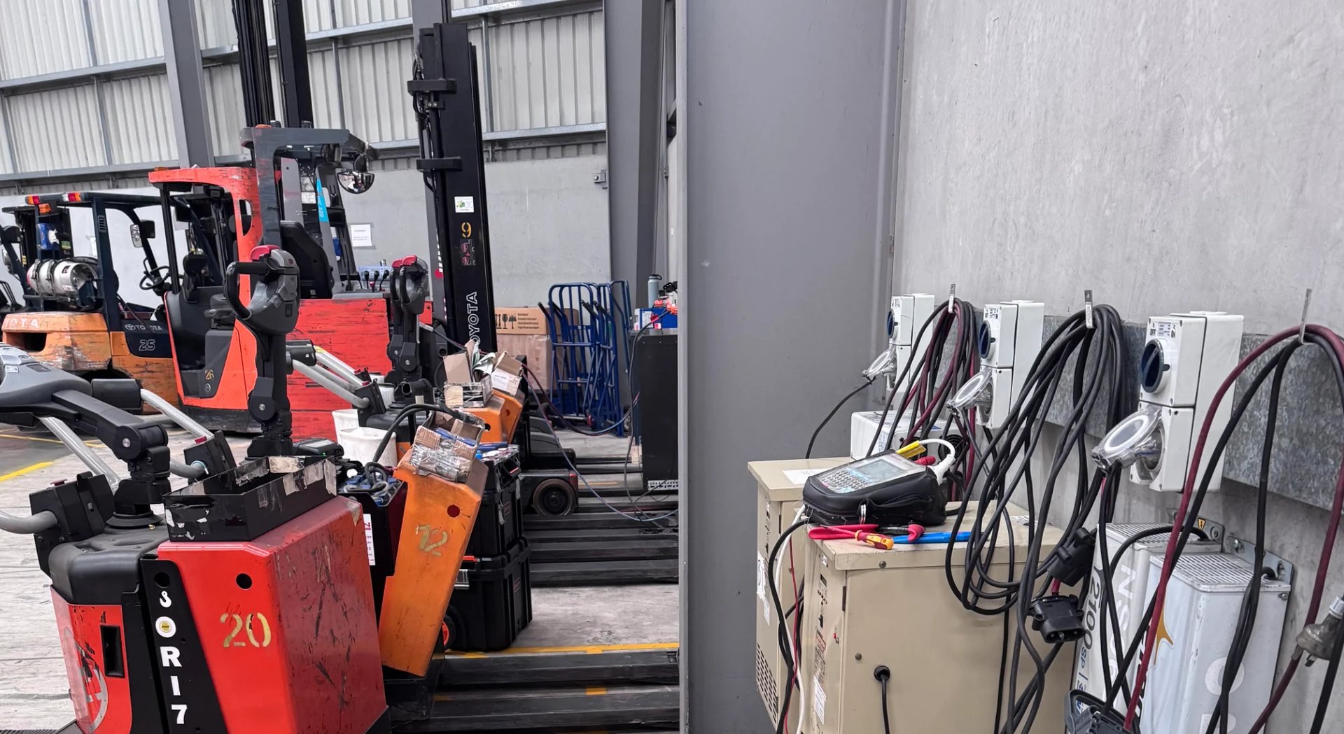 Red and orange forklifts parked indoors with coiled hoses and equipment on storage shelves
