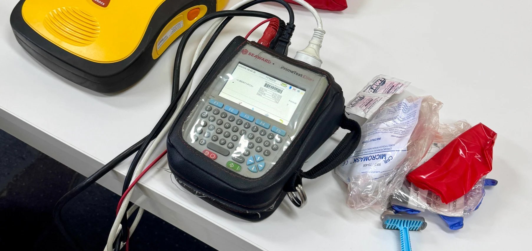 Payment card reader with cables, yellow device, and hardware supplies on white surface