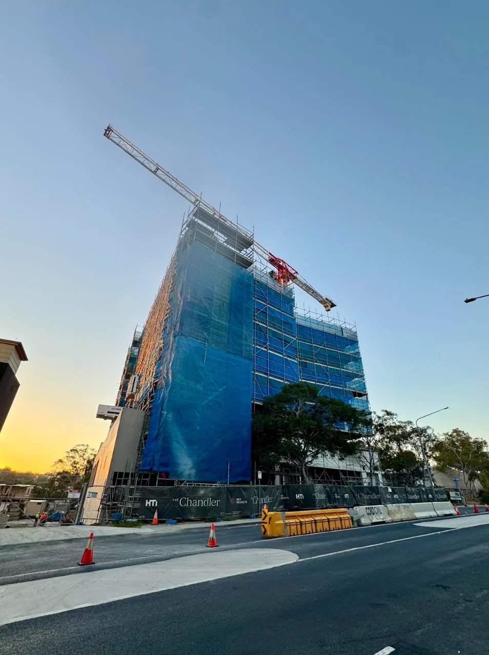 Large commercial building under construction with blue scaffolding and crane at sunset