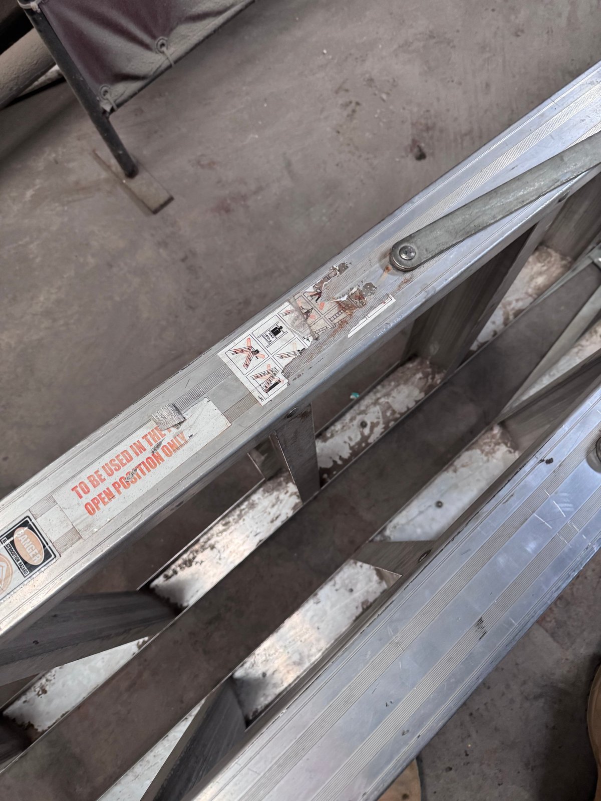 Close-up of worn metal ladder or extension beam with rust stains and weathered aluminum frame on concrete surface