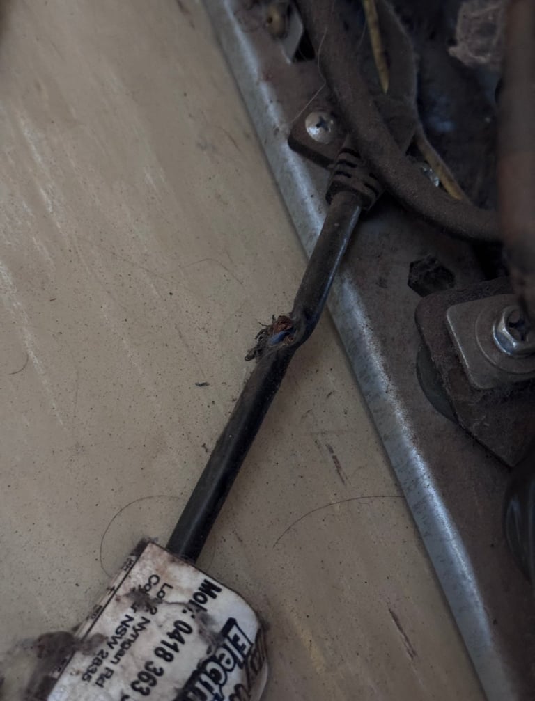 Close-up of an old, corroded metal brake cable or wire attached to vehicle hardware with a worn metal label tag