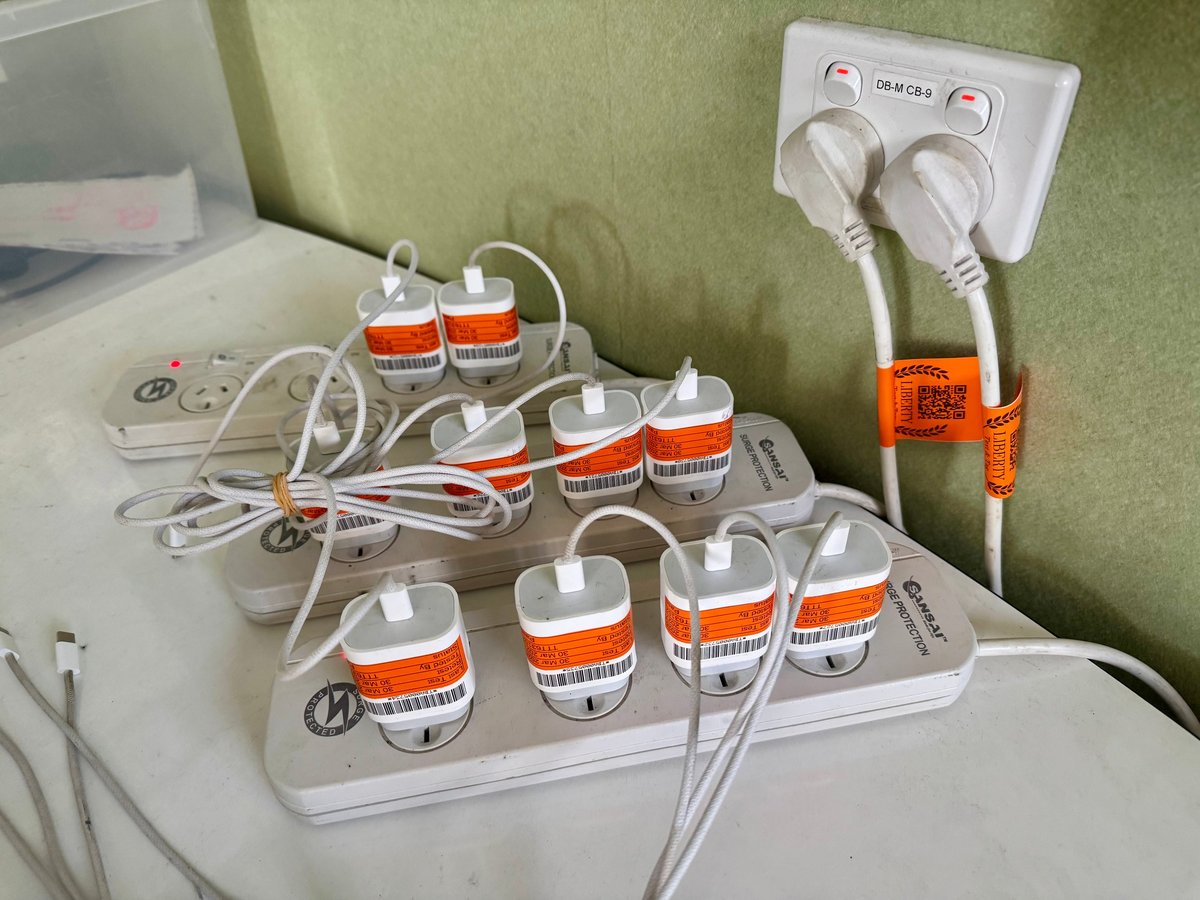 Multiple white power strips with orange-labeled outlets and tangled cords on a table against a green wall